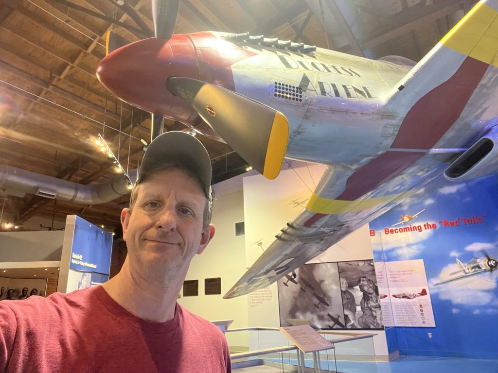 RoamingMonk standing beneath the P-51 Mustang exhibit at Tuskegee Airmen National Historic Site