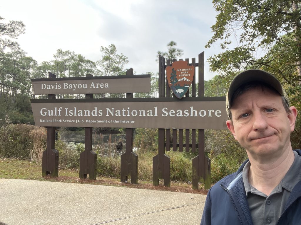 Gulf Islands National Seashore Visitor Center: Davis Bayou Guide 2 A sign for Gulf Islands National Seashore Davis Bayou Area, with a man standing to the right.