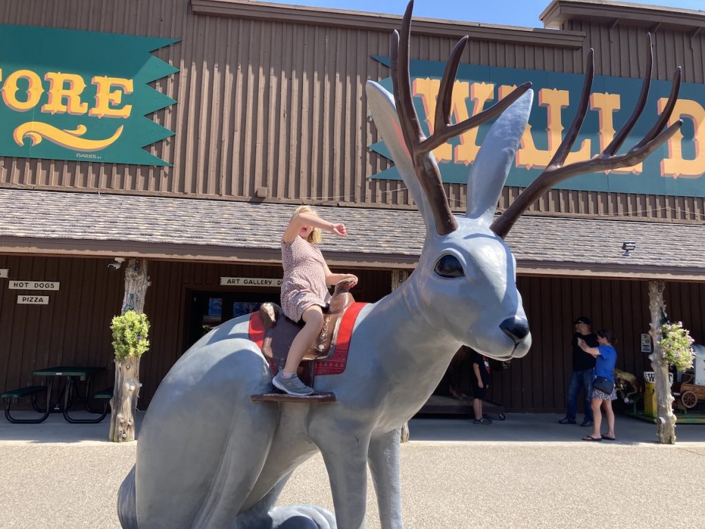 Girl with hands up sitting on a giant grey Jackalope at Wall Drug SD