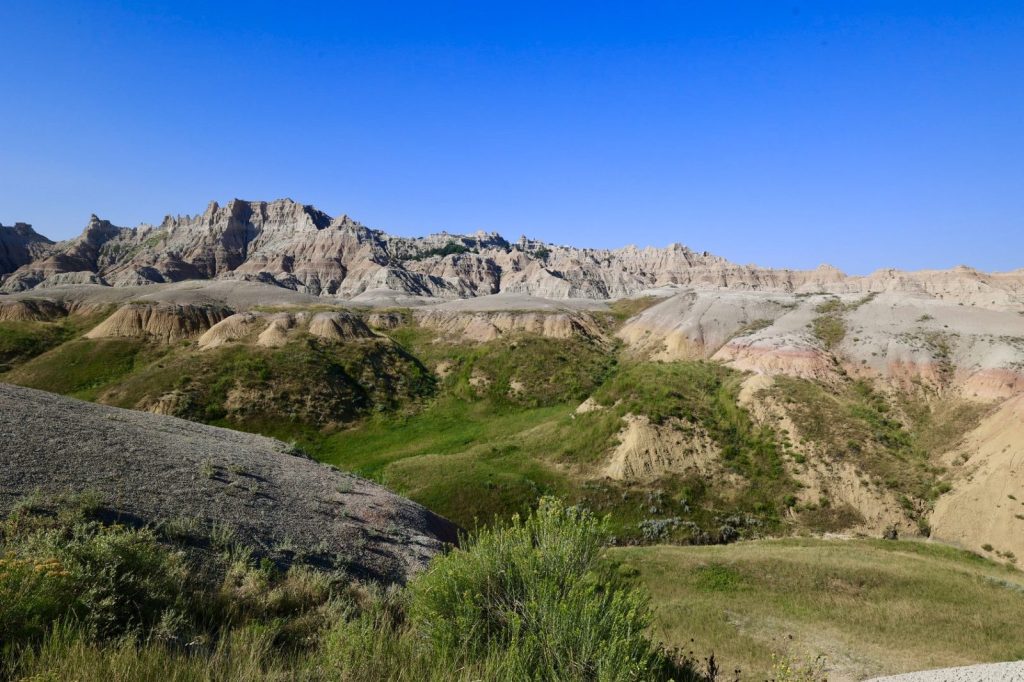 Jagged Badlands buttes with green scrub vegetation under a vivid blue sky