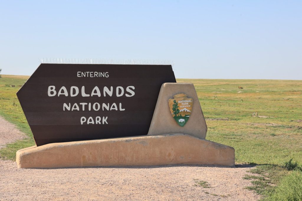 Entering Badlands National Park sign with flat grasslands stretching into the distance
