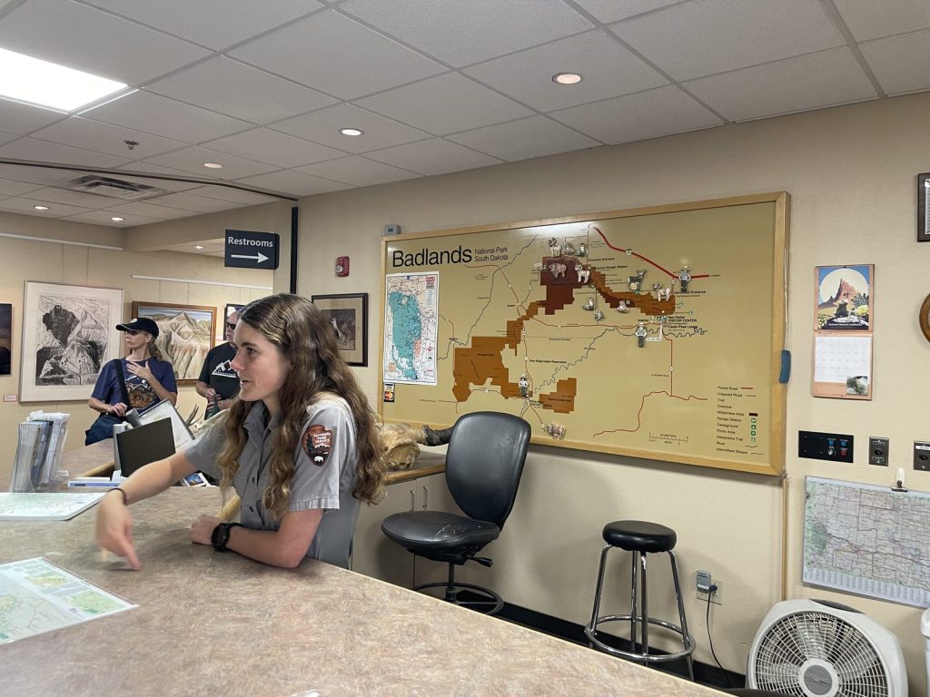 Park ranger at the information desk inside Ben Reifel Visitor Center with Badlands map on the wall