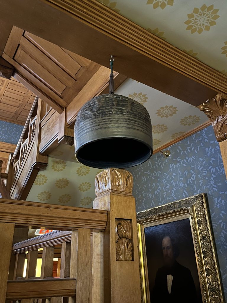 Bronze bell in the Lawnfield stair hall with portrait visible below at Garfield NHS