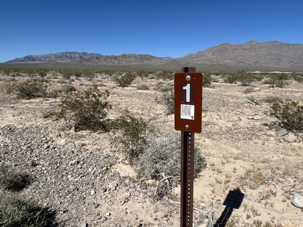 Numbered trail stop marker number 1 with QR code in desert scrubland at Tule Springs Fossil Beds with Spring Mountains in background