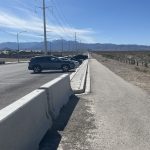 Car parked in street-side pull-off along jersey barrier at Tule Springs Fossil Beds National Monument with mountains in background