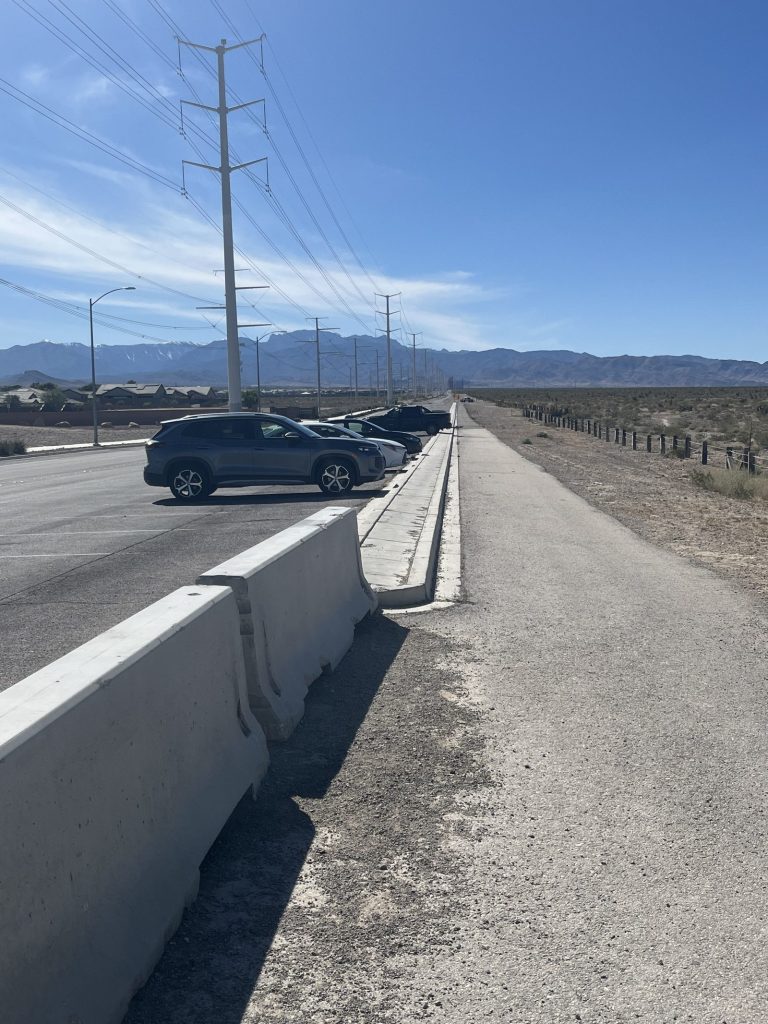 Car parked in street-side pull-off along jersey barrier at Tule Springs Fossil Beds National Monument with mountains in background