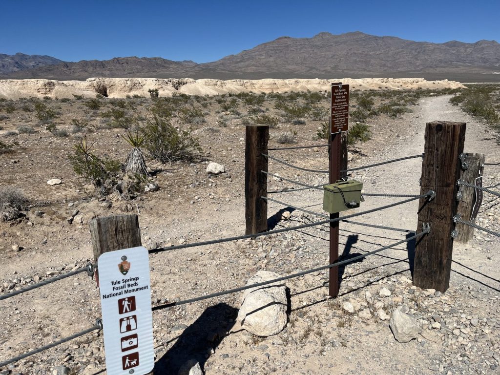 Trail entrance gate with rope and wooden post fencing at Tule Springs Fossil Beds National Monument with white fossil bed cliffs visible behind